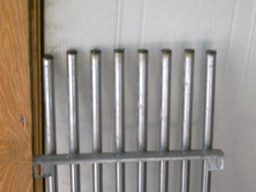 Row of vertical steel tubes welded to a flat bar leaning against a white wall, fabricated rack
