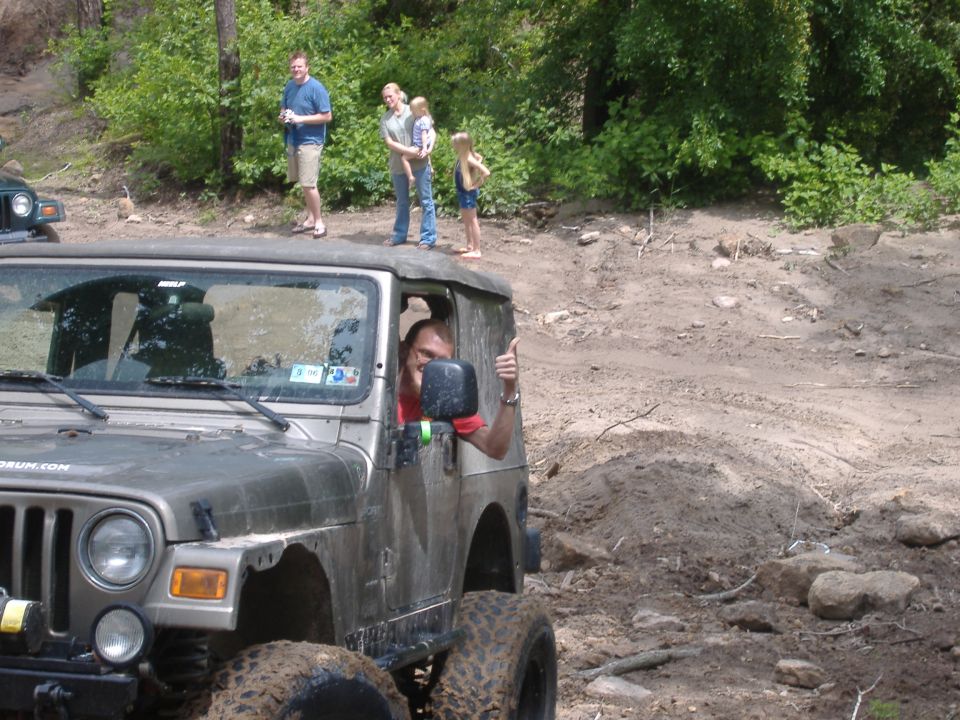 Silver Jeep Wrangler with driver giving thumbs up, off-road scene