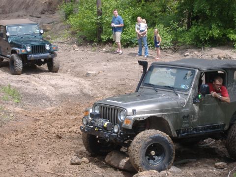 2004 Jeep Wrangler - Two Jeep Wranglers navigate a challenging muddy off-road course on a sunny day.