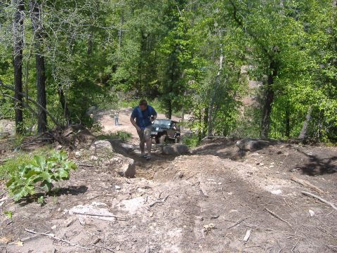2004 Jeep Wrangler - A man walks near a Jeep TJ navigating a rocky off-road trail in a wooded area.