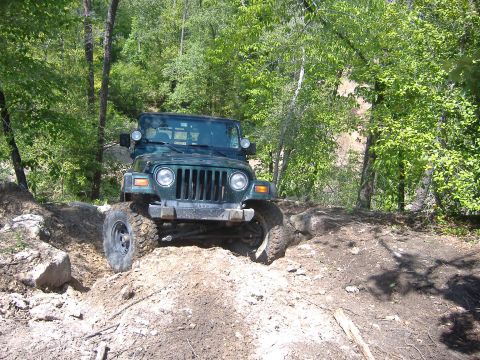 2004 Jeep Wrangler - A green 2004 Jeep TJ is shown tackling a challenging off-road course with steep inclines and rocks.