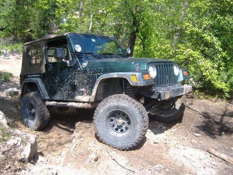 2004 Jeep Wrangler - A green Jeep TJ navigates a rocky, off-road trail, kicking up dirt.