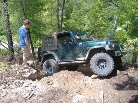 2004 Jeep Wrangler - A man watches a green 2004 Jeep TJ navigate a challenging dirt trail with large tires.