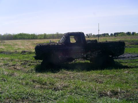 1994 Ford F-250 - A pickup truck is covered in mud while sitting in a grassy field under a clear sky.