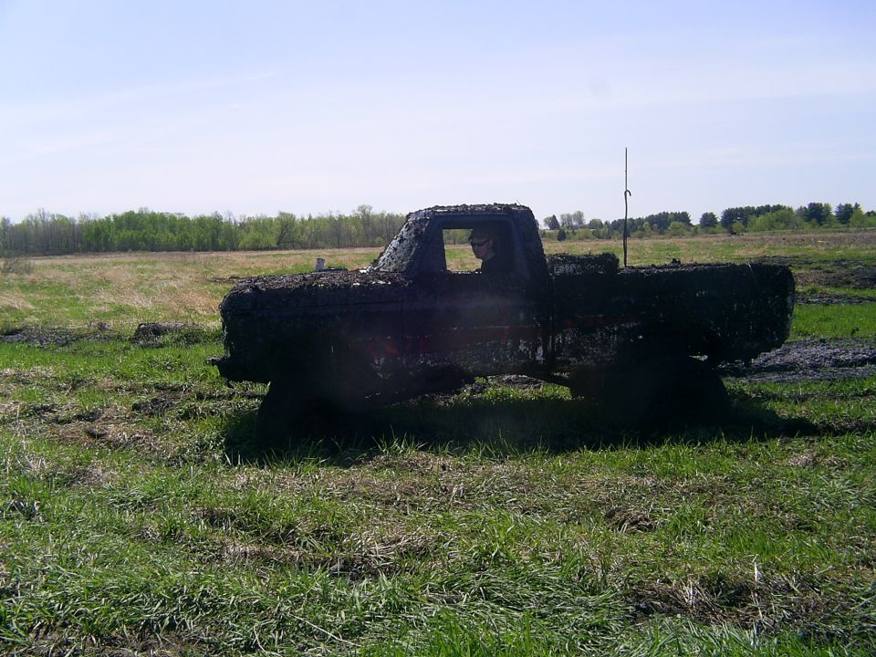 Mud-covered pickup truck stuck in a grassy field with trees in the background