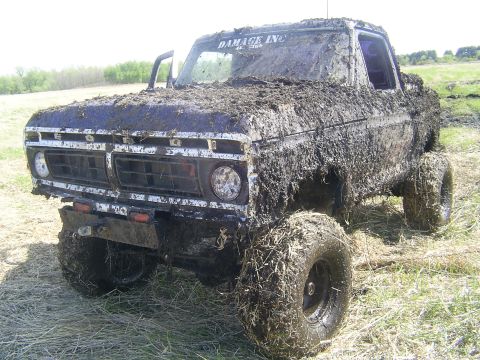 1994 Ford F-250 - A heavily mud-caked pickup truck sits in a grassy field, its front end angled towards the camera.