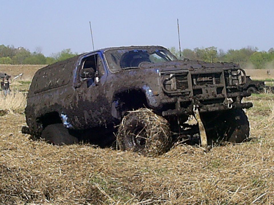 Mud-covered GMC SUV stuck in a grassy field, front grille visible