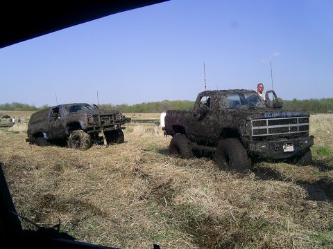 1994 Ford F-250 - Muddy trucks are stuck in a field under a clear blue sky.