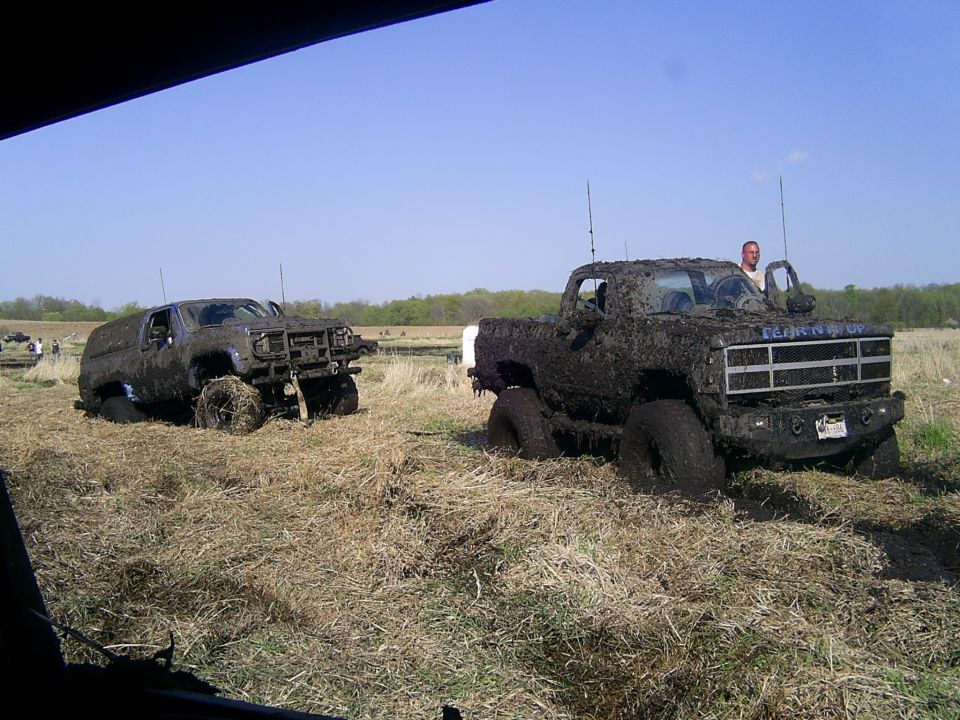 Two trucks stuck in mud, one is a pickup with a man standing by the open door
