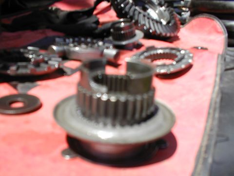 1979 Ford Bronco - Various metal gears and parts are spread out on a red surface, likely for automotive repair or assembly.
