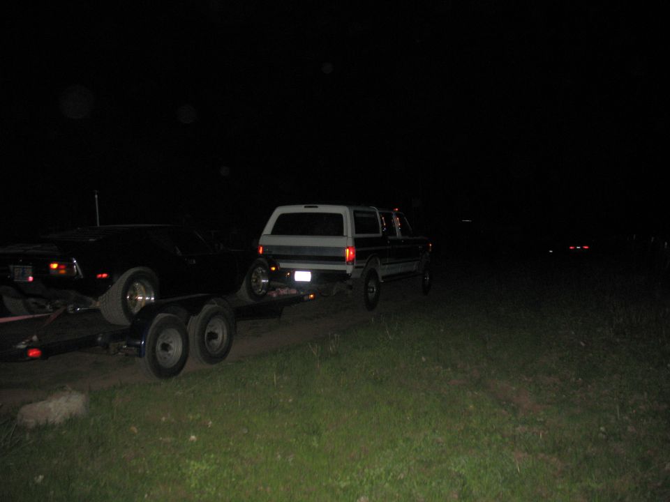 Dark sports car on flatbed trailer towed by pickup truck at night on grass