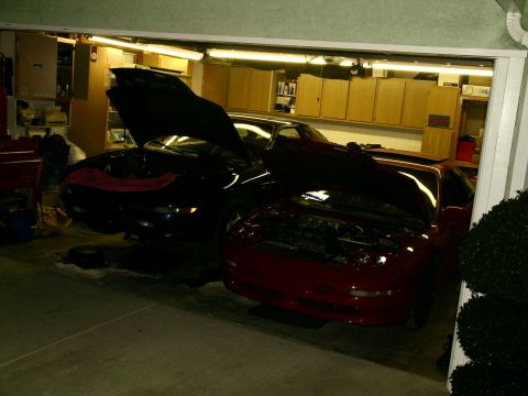 1995 Ford Probe - Two cars, one red and one dark blue, are parked in a garage with their hoods open, suggesting maintenance or a project.