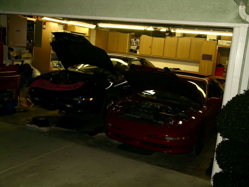 Two cars with hoods open in a garage, one red and one dark blue