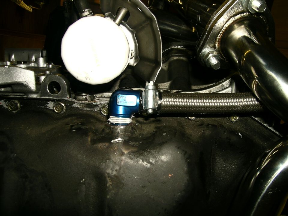 Engine oil pan with blue fitting and braided oil line, white oil filter visible