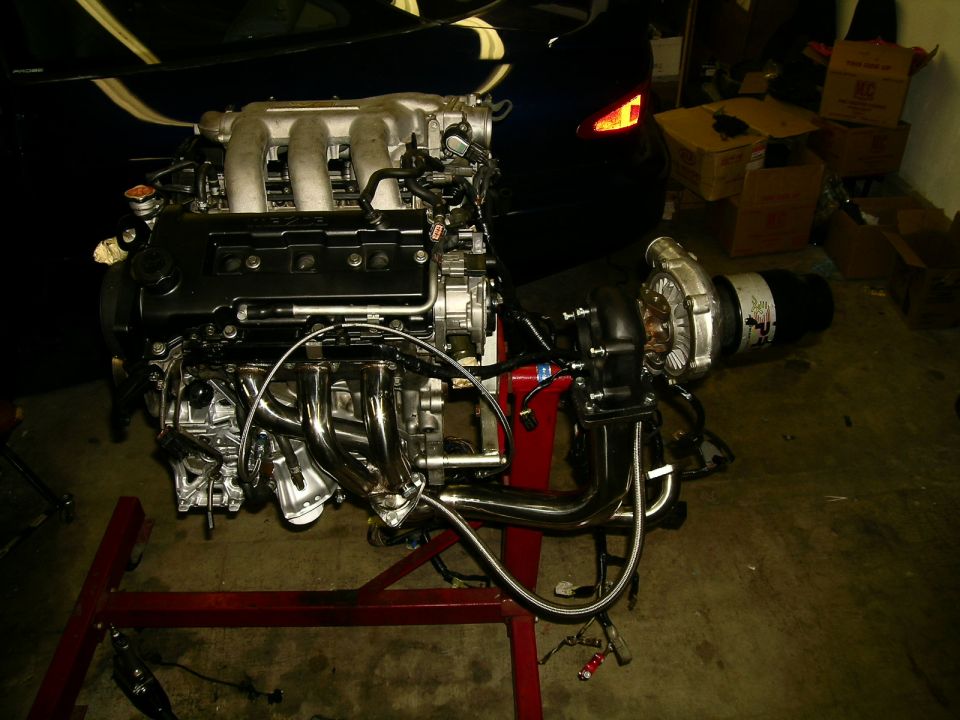 Turbocharged engine assembly on a red stand, with part of a dark car in the background