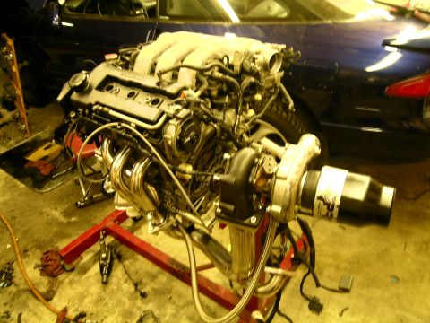 1995 Ford Probe - Engine assembly with turbocharger, mounted on a stand, with a dark blue vehicle behind it.
