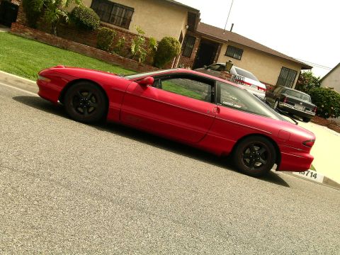 1993 Ford Probe - Red 1993 Ford Probe parked curbside in front of a house with other vehicles visible.