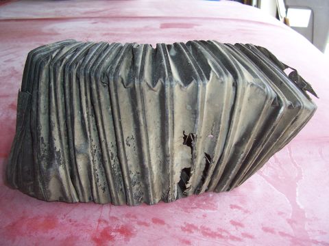 1978 Ford Bronco - A damaged, dusty rubber duct part is shown close-up against a red background.