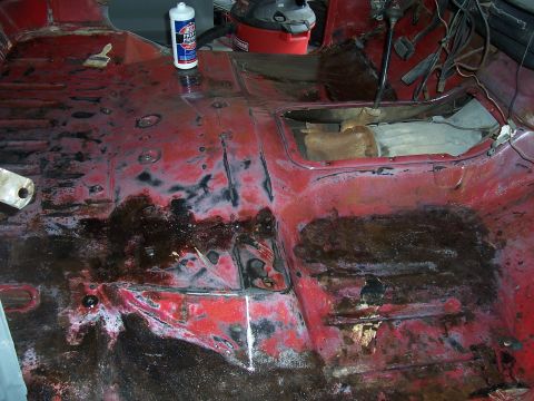 1978 Ford Bronco - The interior floor of a vehicle shows significant rust and damage, with cleaning supplies present.