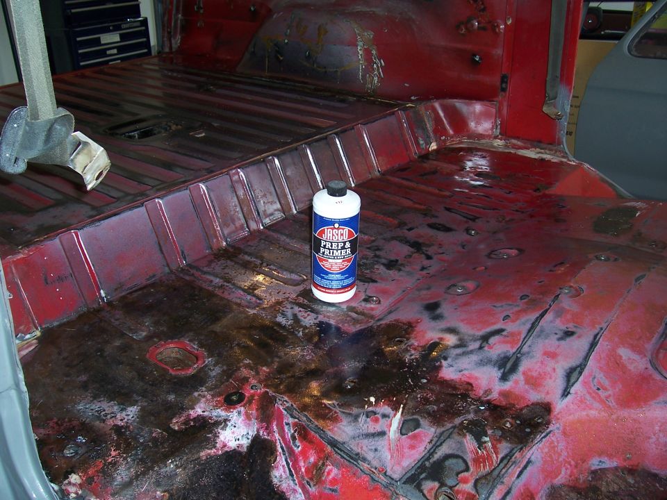 Interior floor pan of a vehicle undergoing restoration, showing rust and a can of Jasco Prep & Primer