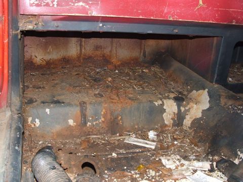 1966 Ford Ranchero - Looking down through an open door opening at the stripped floorpan of a red project car, with seats and carpet removed to reveal surface-ru…