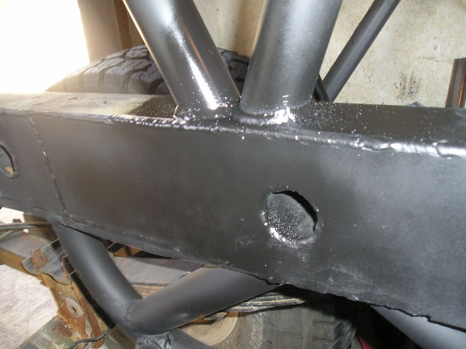Black painted vehicle frame with welded roll cage tubes, tire visible in background