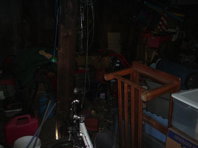 Cluttered storage area with a bicycle, red gas can, wooden furniture, and various boxes