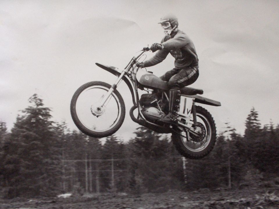 Motocross rider airborne over trees, wearing helmet and goggles, on a dirt bike