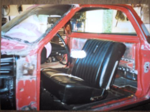 1968 Ford Ranchero - Interior view of a red vehicle with a black bench seat and exposed door panels, suggesting it is in a state of repair.
