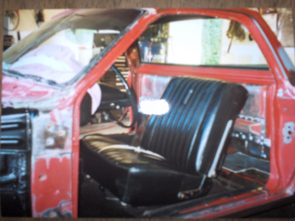 Red car interior showing a black vinyl bench seat, dashboard, and door panel. The vehicle appears to be undergoing restoration