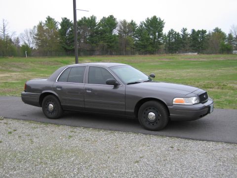1991 Ford LTD Crown Victoria - A dark gray Ford Crown Victoria sedan is parked outdoors on a paved path next to a gravel area.