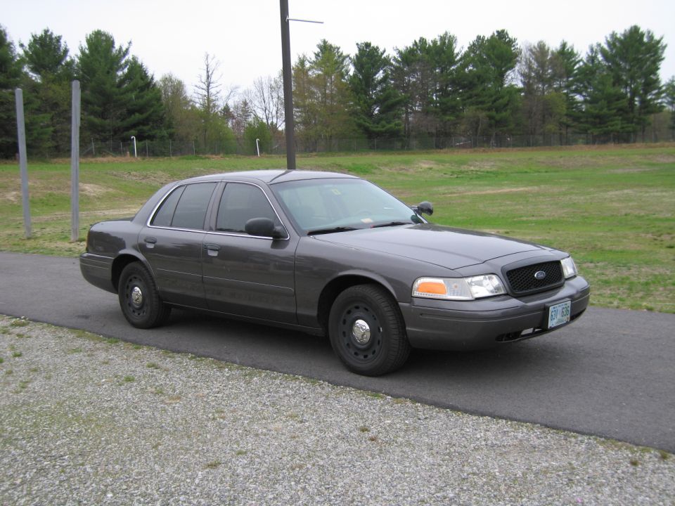 Dark gray Ford Crown Victoria sedan parked on asphalt, front 3/4 view. License plate visible