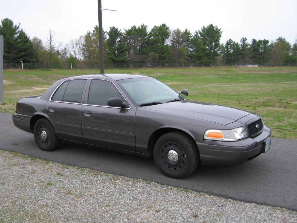 Dark gray Ford Crown Victoria parked on asphalt next to a gravel shoulder