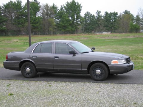 1991 Ford LTD Crown Victoria - A gray Ford Crown Victoria sedan is parked on a paved surface with a gravel shoulder and a grassy field in the background.