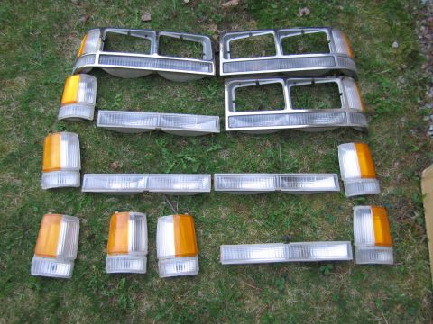 1991 Ford LTD Crown Victoria - Assorted car lighting components and front grille sections are displayed on a grassy surface.