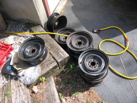 1991 Ford LTD Crown Victoria - A collection of used steel wheels are piled up outdoors next to a building.
