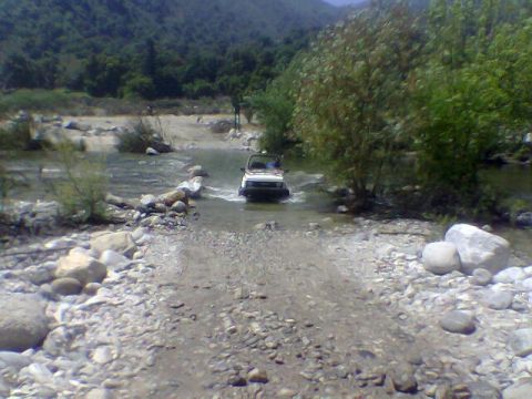1988 Ford Bronco - A white SUV navigates a shallow, rocky river in a natural landscape.