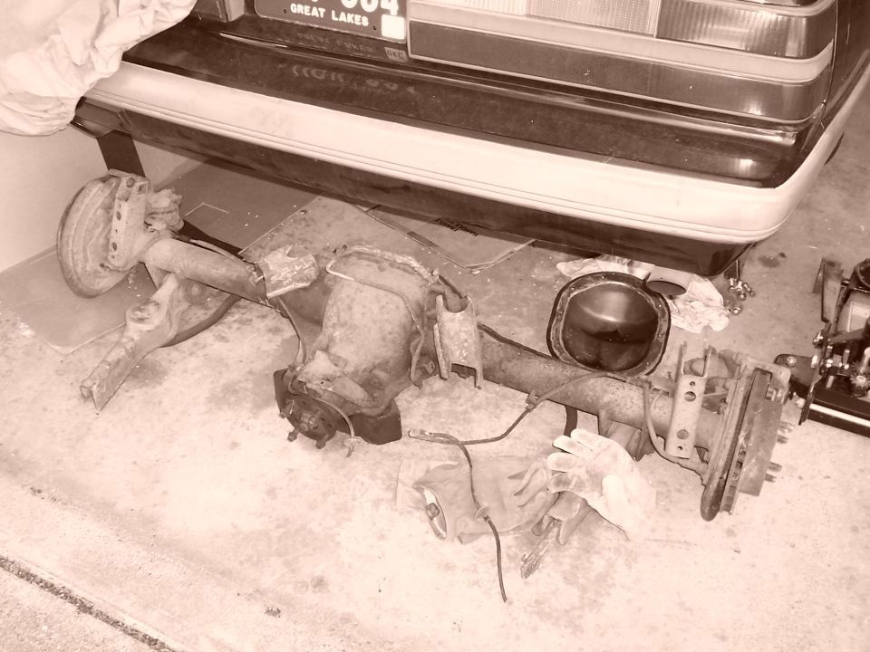 rear axle assembly removed from a car, sitting on the ground under the car's rear bumper