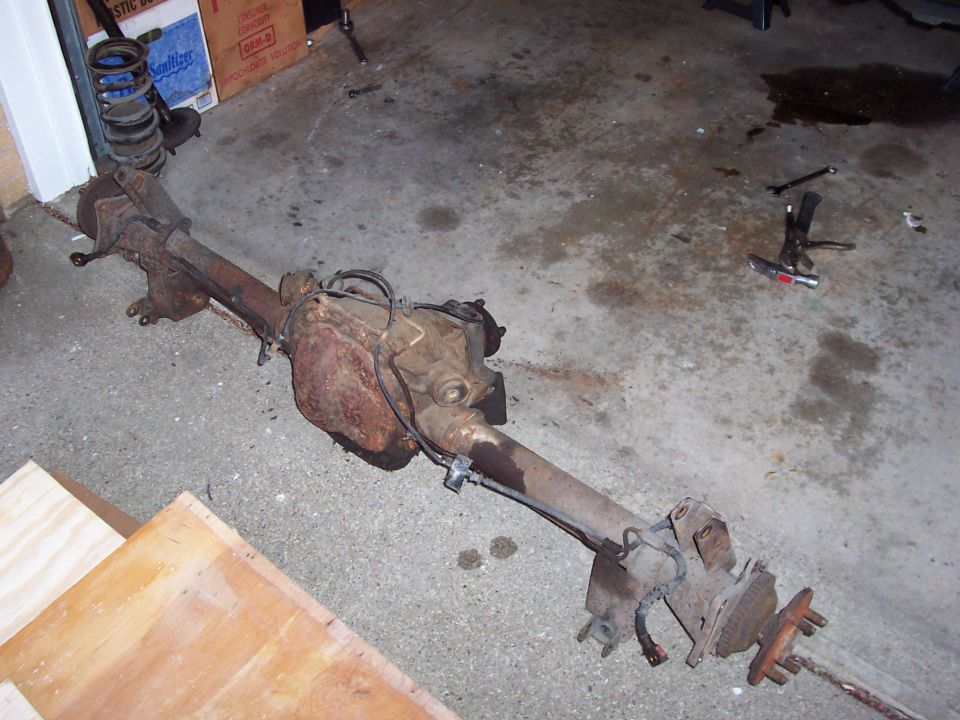 Rusty rear axle assembly with differential and brake components on concrete floor