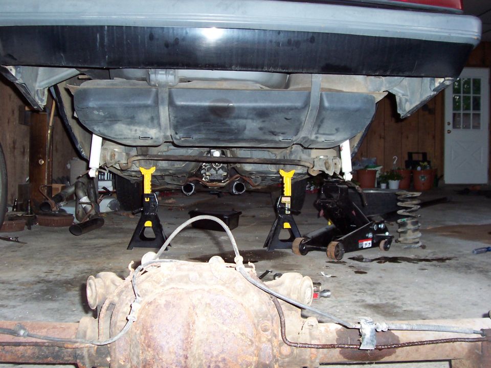 Car's rear axle and fuel tank on jack stands, with a floor jack nearby