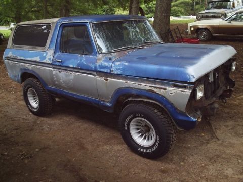 1978 Ford Bronco - Three-quarter front view of a faded blue and silver two-tone late-1970s Ford Bronco project truck parked on dirt, with the front bumper and…