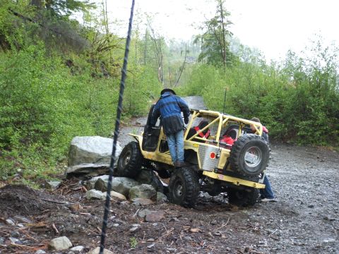1980 Ford Bronco - A yellow off-road vehicle with a roll cage is seen from the rear as it maneuvers over rocks on a muddy trail.