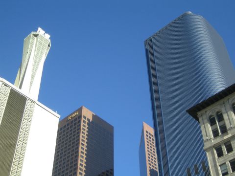 1968 Ford Mustang - Modern skyscrapers dominate the urban landscape under a bright blue sky.