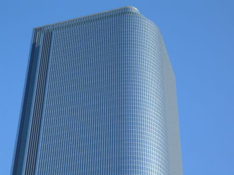 1968 Ford Mustang - A modern glass skyscraper with a curved facade stands tall against a bright blue sky.