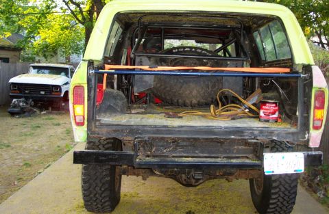 1978 Ford Bronco - Rear view of a yellow 1978 Ford Bronco with its tailgate open, showing a spare tire and other items.