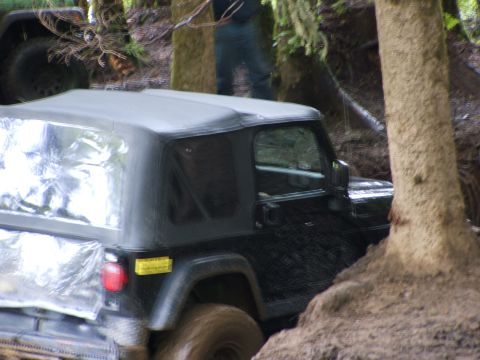 1980 Ford Bronco - Jeep Wrangler TJ on a challenging off-road trail with muddy terrain and trees.