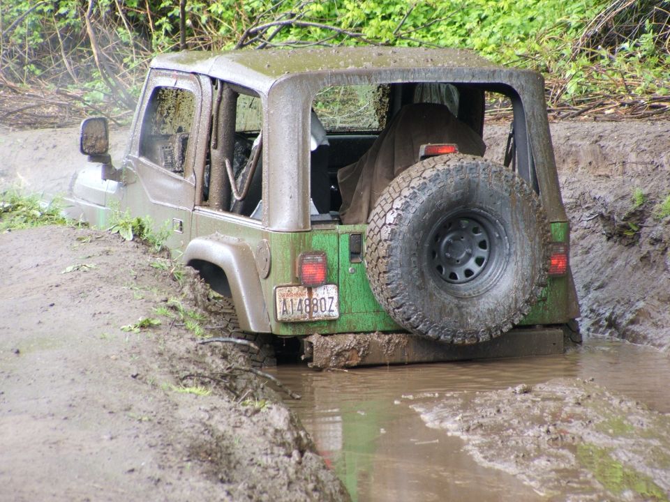 Green Jeep Wrangler stuck in mud, rear view with spare tire mounted