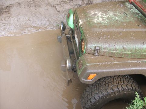 1980 Ford Bronco - A muddy off-road vehicle navigates through a water-filled ditch.