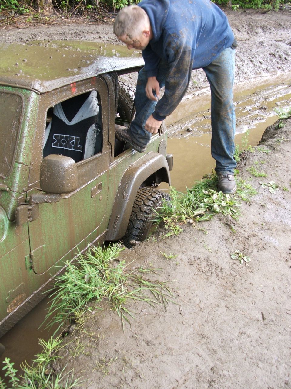 Green Jeep Wrangler stuck in mud with a person stepping into it