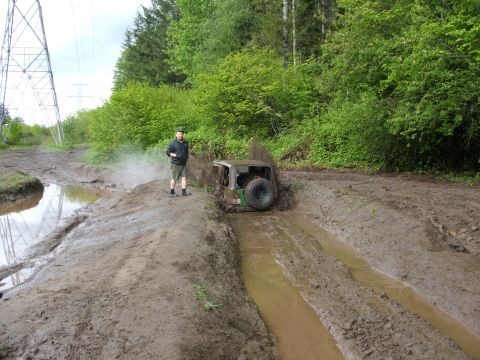 1980 Ford Bronco - A person stands by an off-road vehicle struggling through a muddy track with trees in the background.